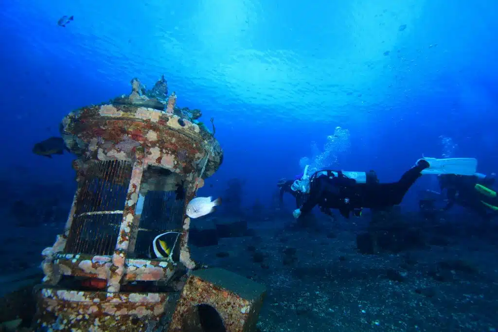 Scuba divers exploring shipwreck dive site in Amed Bali with coral covered wreck