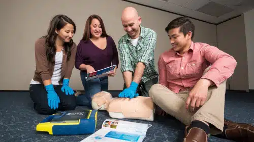 Students completing EFR/Rescue course with instructor stood around dummy body practicing CPR