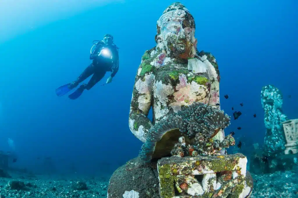 Underwater statue at Amed Bali dive site with scuba diver exploring coral reef