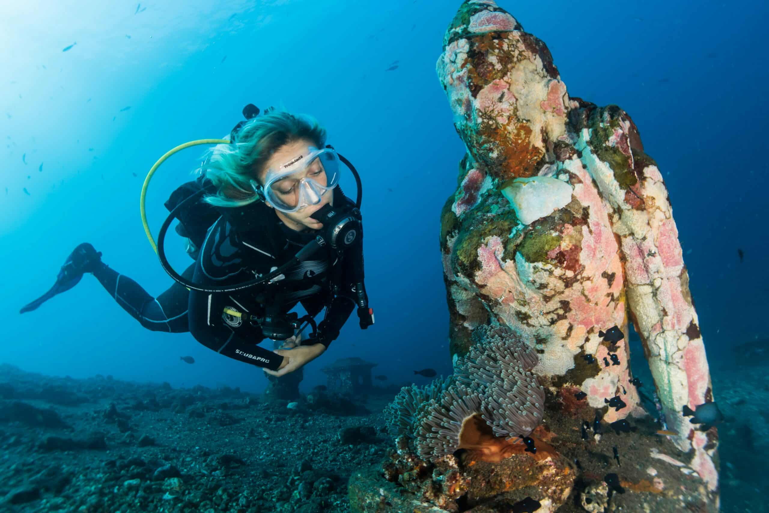 Scuba diver next to underwater statue in Amed Bali dive site with coral growth
