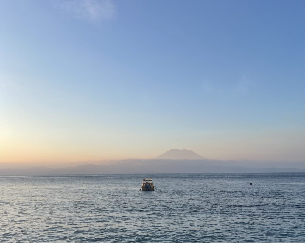 Peaceful sunset over the Bali Sea, featuring a small fishing boat and Mount Agung on the horizon