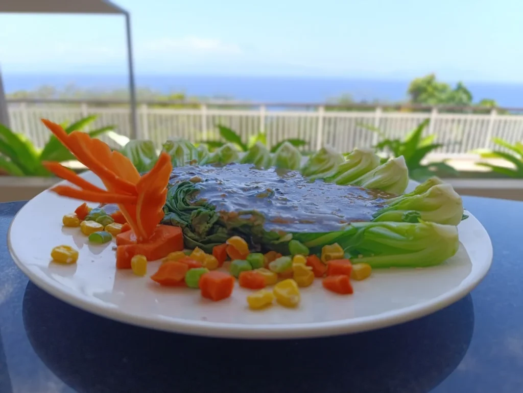 Plated vegetarian dish with leafy greens and mixed vegetables overlooking the ocean in Nusa Penida