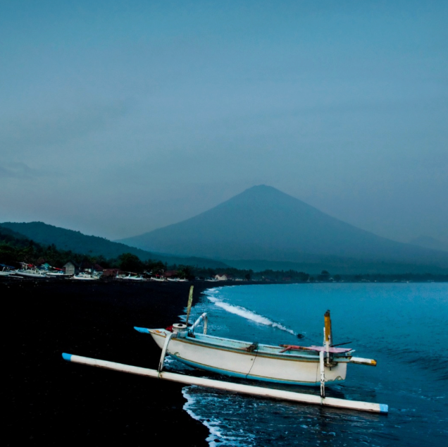 Traditional jukung fishing boat on Amed Beach with Mount Agung in the background, showcasing the stunning coastline near Jukung Dive Resort in East Bali.