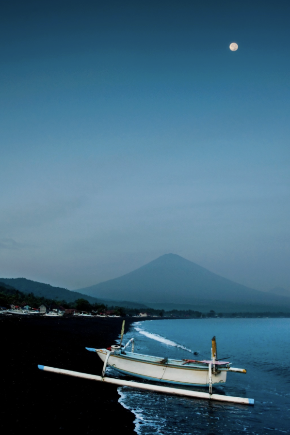 Traditional jukung fishing boat on Amed Beach with Mount Agung in the background, showcasing the stunning coastline near Jukung Dive Resort in East Bali.