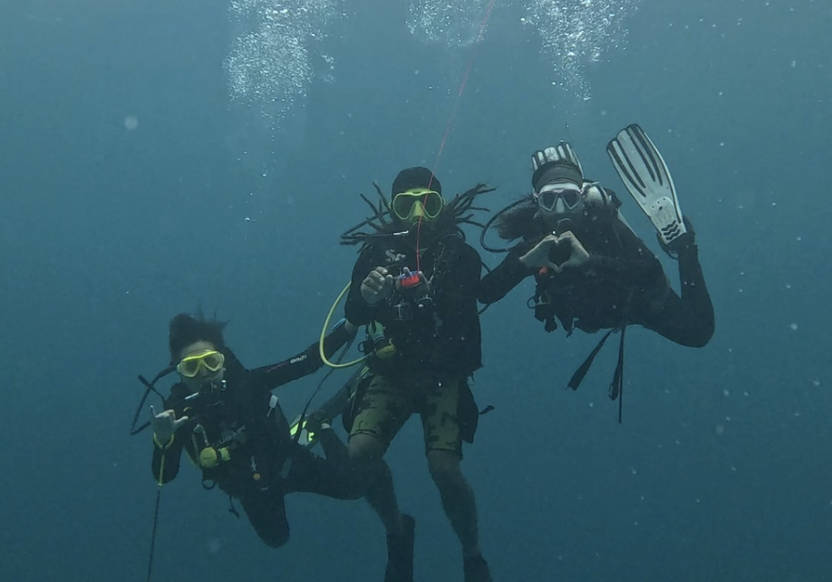 Group of three scuba divers during safety stop smiling, looking happy, and making a love heart with SMB